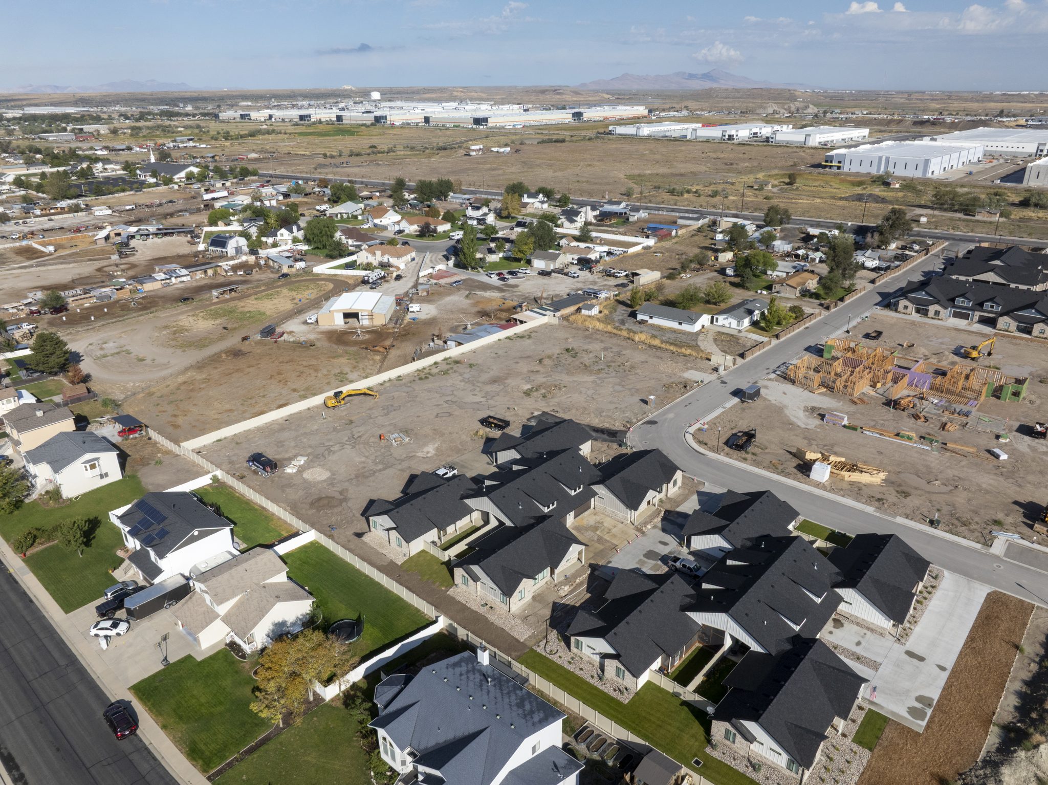 Aerial view of a Utah twin home development with finished units, framed homes under construction and an excavator on open lots